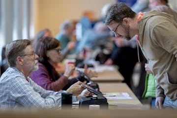Poll volunteer Craig Erickson, left, checks in voter John Moen, right, along with other voters at Advent Lutheran Church in Roseville, Minn., on Tuesd