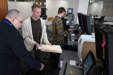 Andrew McGillivary, right, election systems program manager for Hennepin County, hands a stack of testing ballots to Seth Gellman, elections assistant